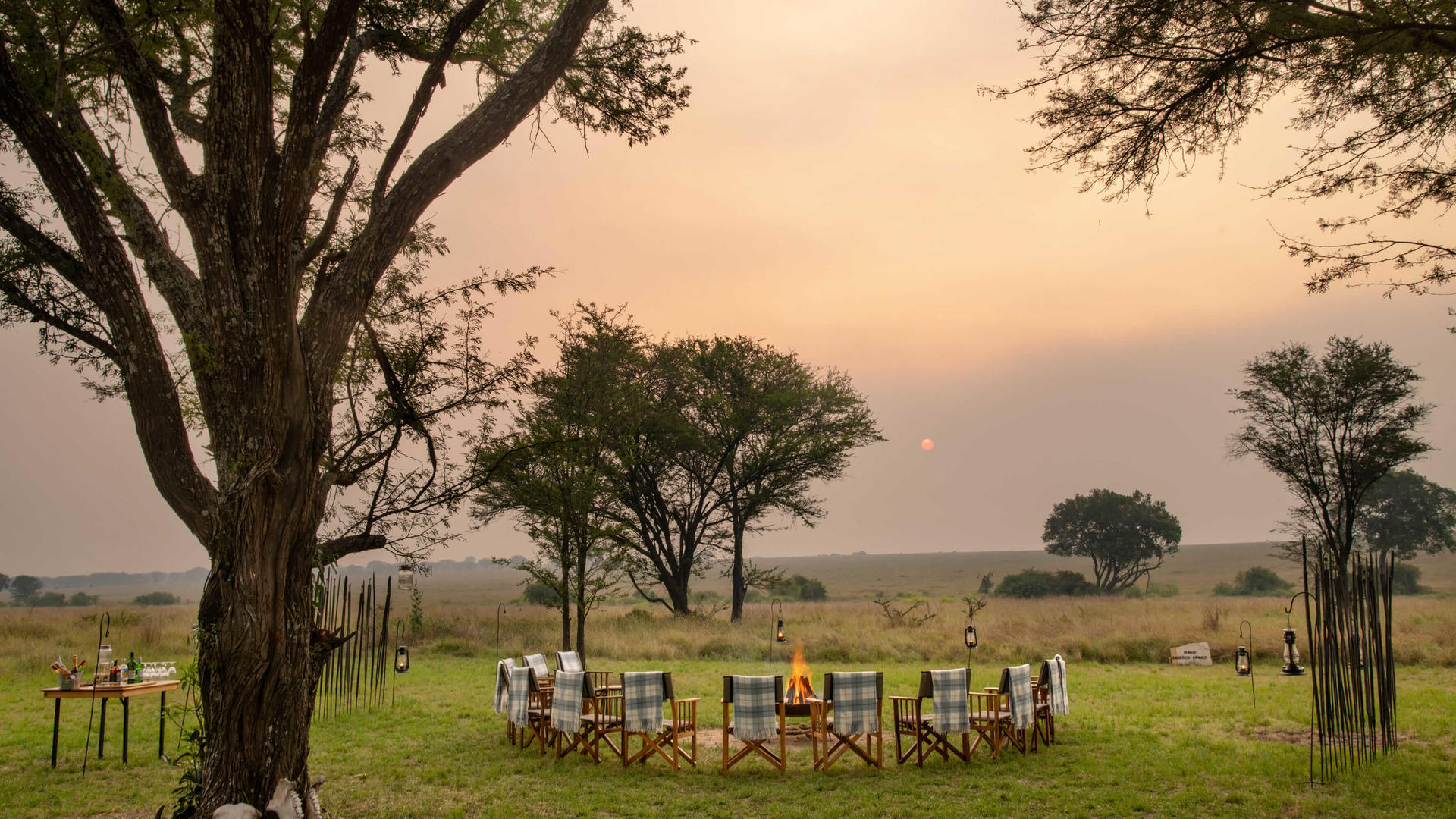 Asilia africa ubuntu migration camp sundowner setup at sunset with fire going