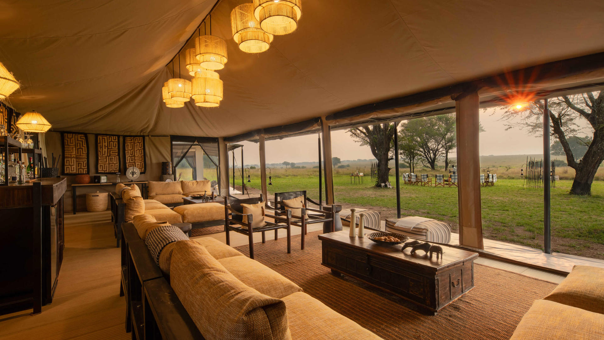Asilia africa ubuntu migration camp main area lit up with sun peaking through at sunset